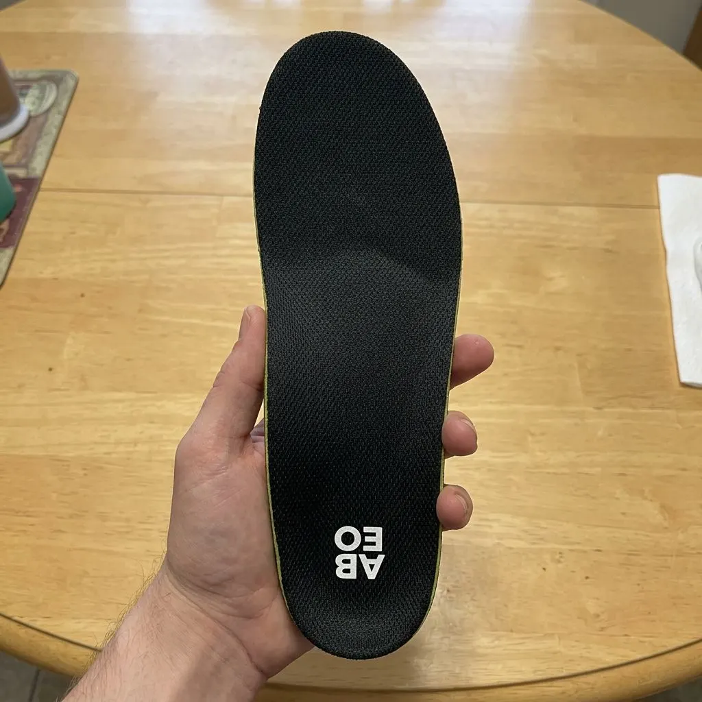 ABEO Premium Orthotic insole held in hand from the underside, showing the ABEO branding and green trim