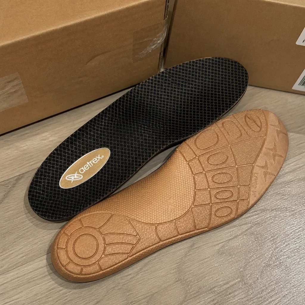 A pair of Aetrex Lynco L400 Compete orthotic insoles next to their retail box on the floor