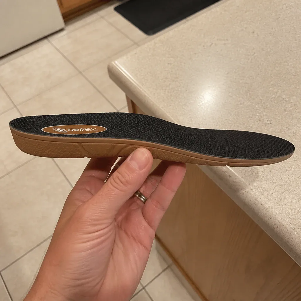 An Aetrex Lynco L400 Compete orthotic insole held sideways, showing its arch profile and thickness