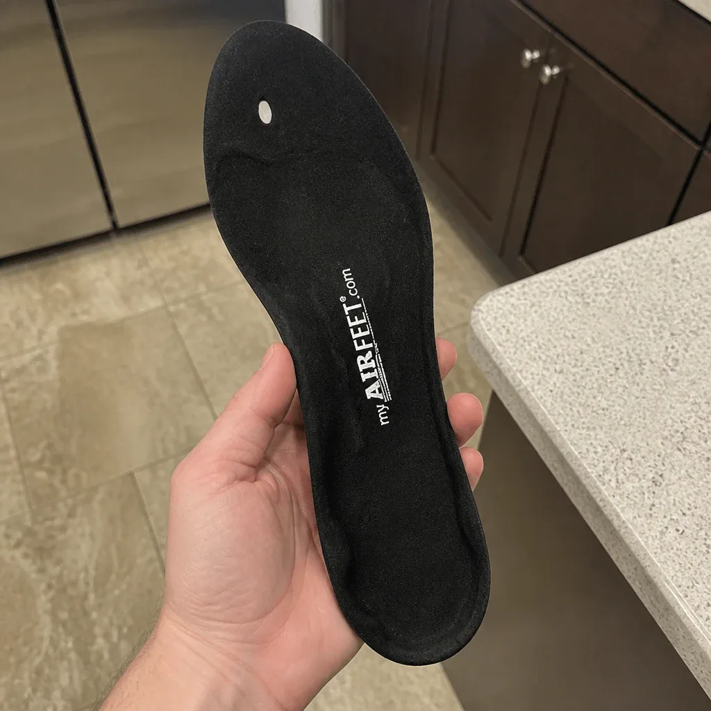 A hand holding an AirFeet Classic O2 insole, showing the gel core and top fabric