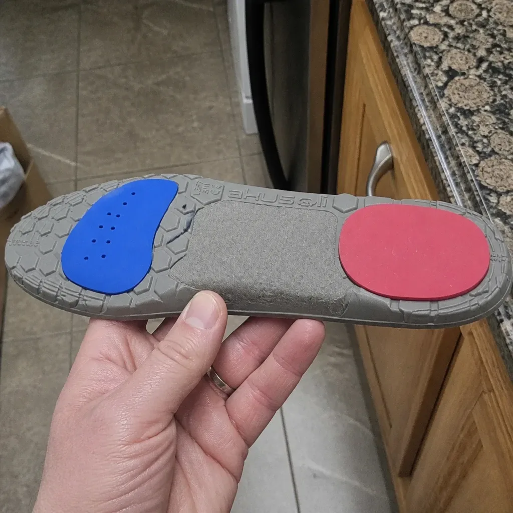 An Akusoli magnetic acupressure insole held sideways, showing the arch profile and heel cup