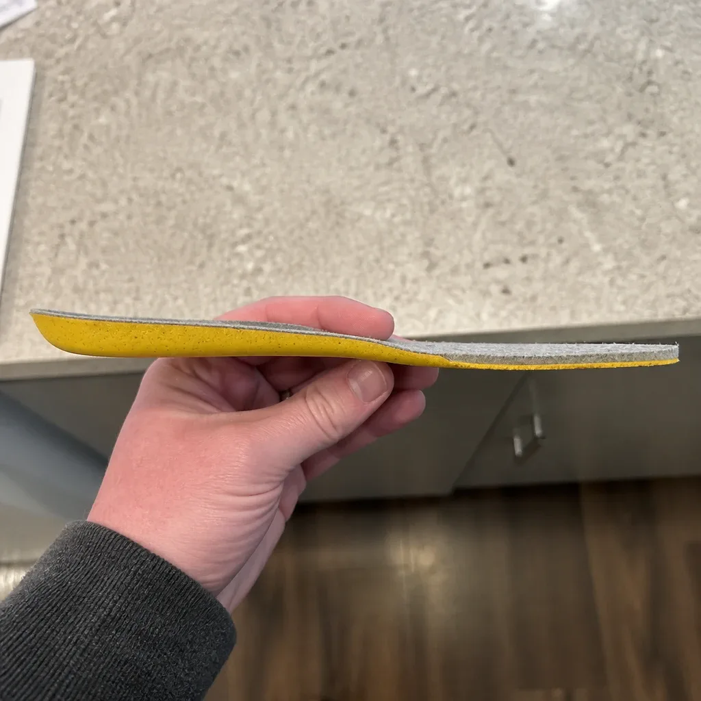 An Allbirds Featherbed insole held sideways in hand, showing its flex and profile