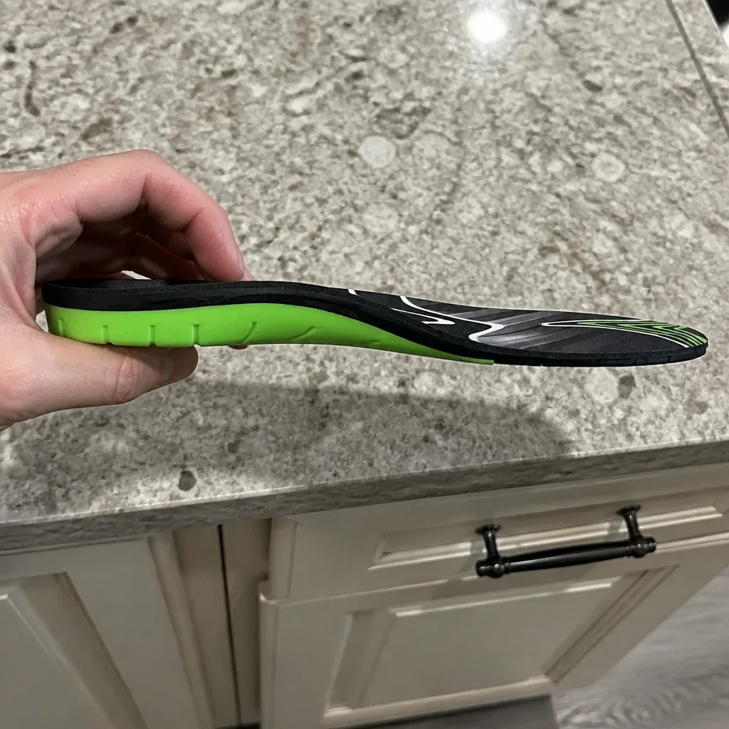 An Apex A-Wave Firm orthotic insole held sideways, showing the arch profile and heel cup