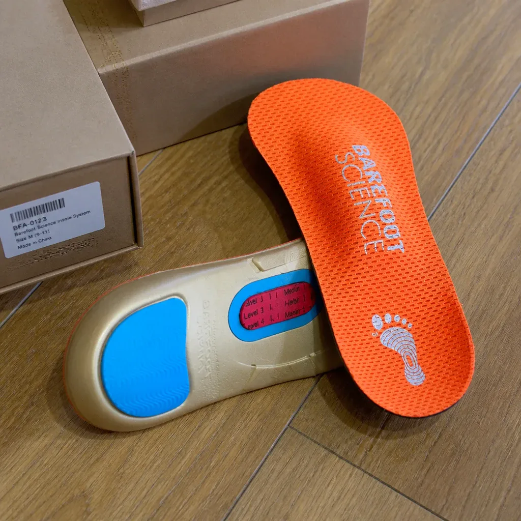 A pair of Barefoot Science insoles next to their retail box on the floor