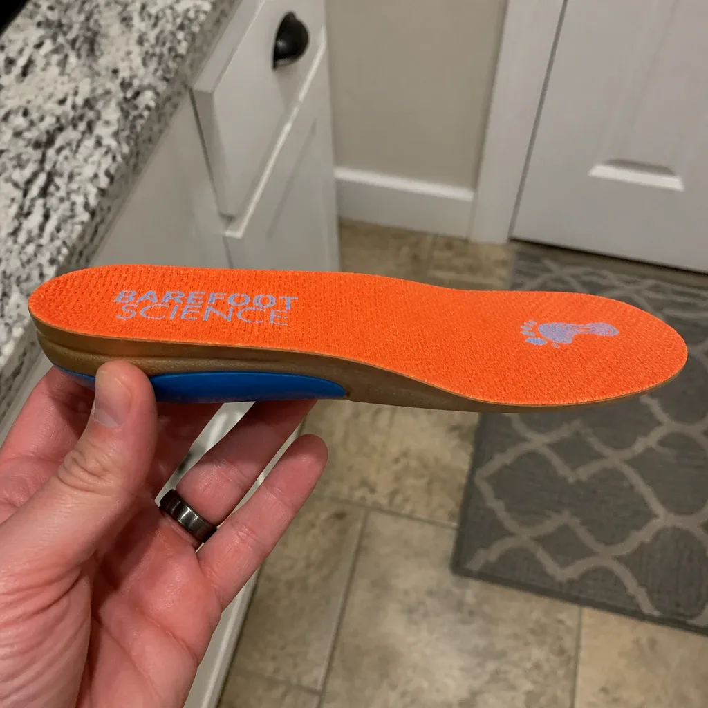 A Barefoot Science insole held sideways, showing the arch shell profile