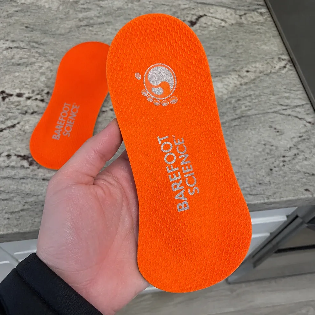 A Barefoot Science insole held in hand, showing the arch plug and heel cup
