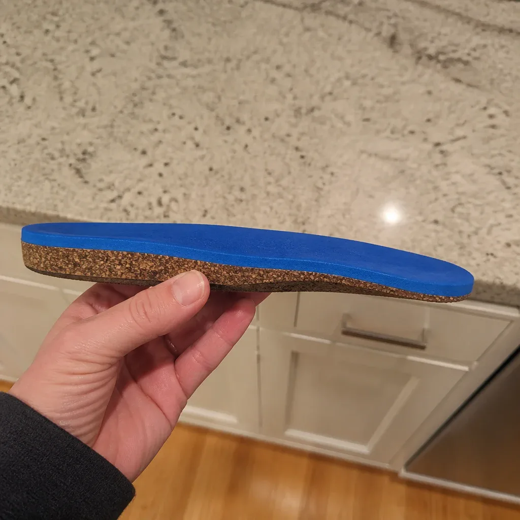 A Birkenstock Birko Sport insole shown from the side, held in hand to display the cork base's profile