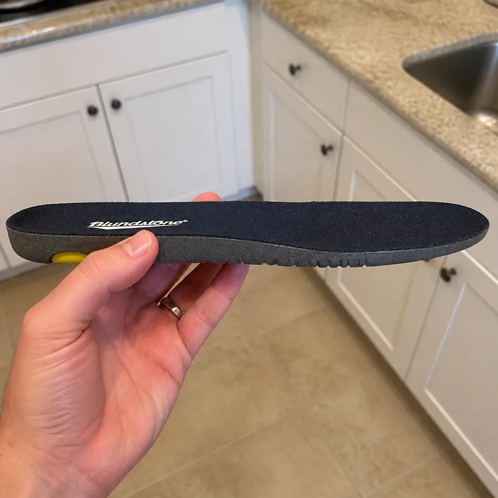 A Blundstone Comfort Classic Footbed insole held sideways, showing the arch profile and heel cup