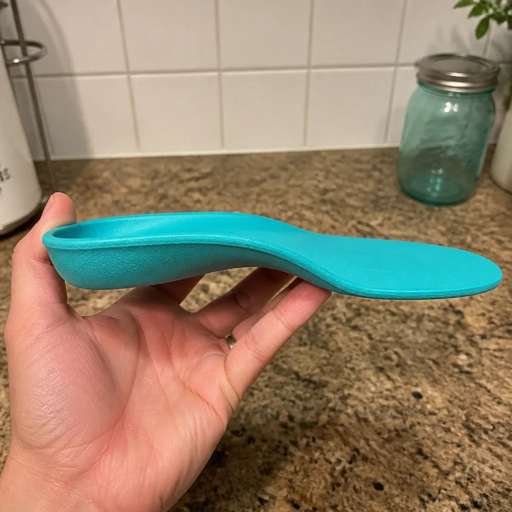 A Comfort Fit Orthotics insole held sideways, showing the arch profile and heel cup