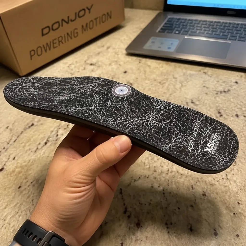 DonJoy insole held sideways in hand showing the heel elevation and shell profile