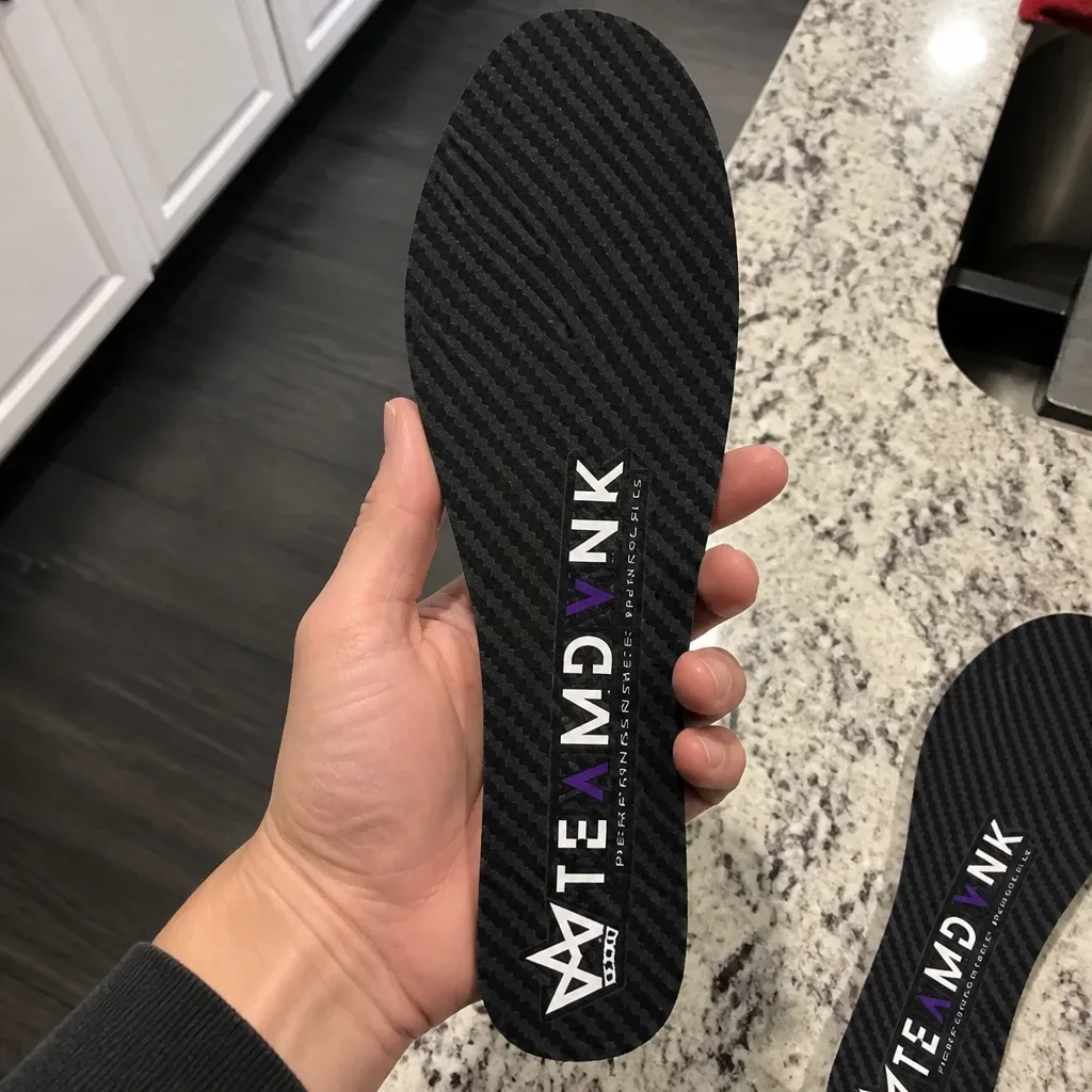 A DVNK carbon fiber insole held in hand, showing the rigid plate and top-cover fabric