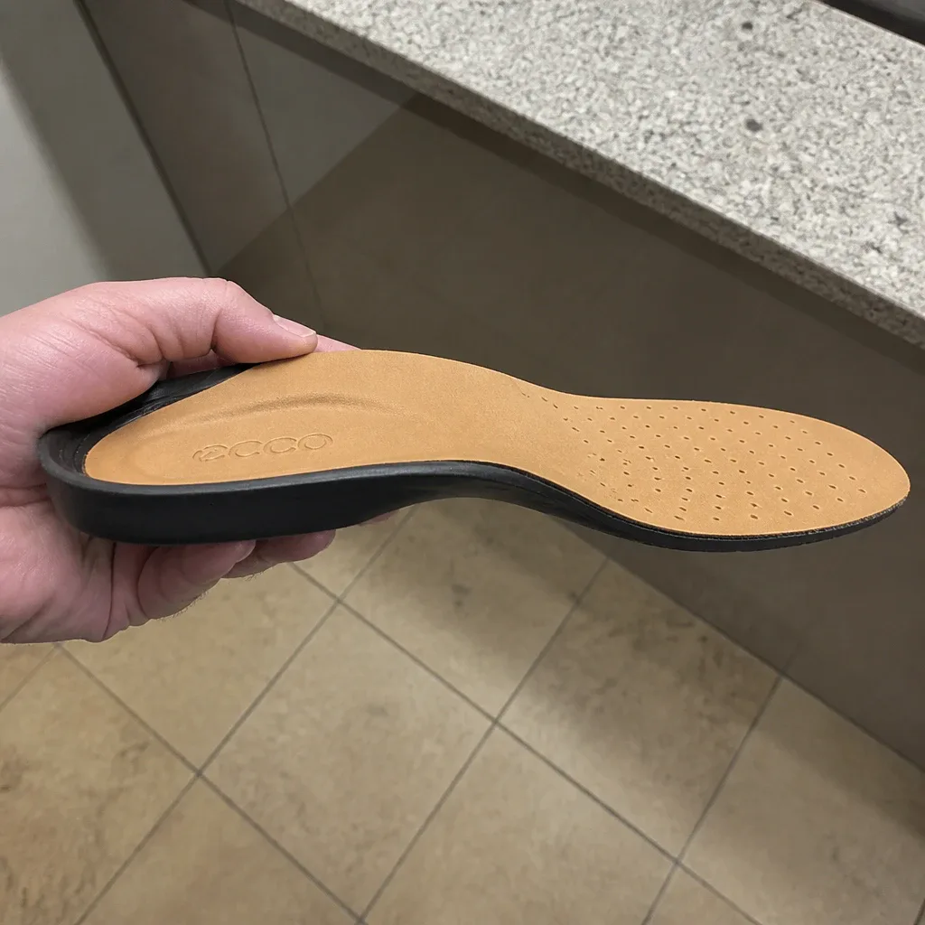 An ECCO Comfort Supreme Leather insole held sideways, showing the arch shelf and heel cup profile