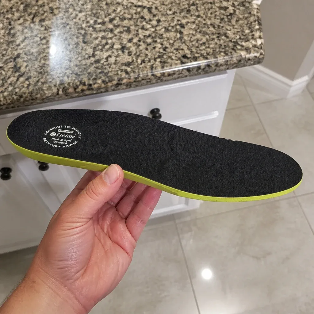 A Fitville Comfort insole held sideways in hand, showing the arch contour and heel depth