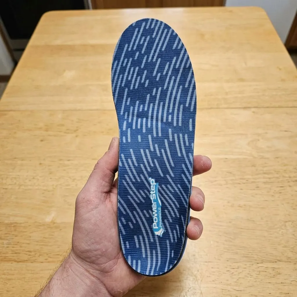 A PowerStep Pinnacle insole held up close, showing the contoured heel cradle and arch shell