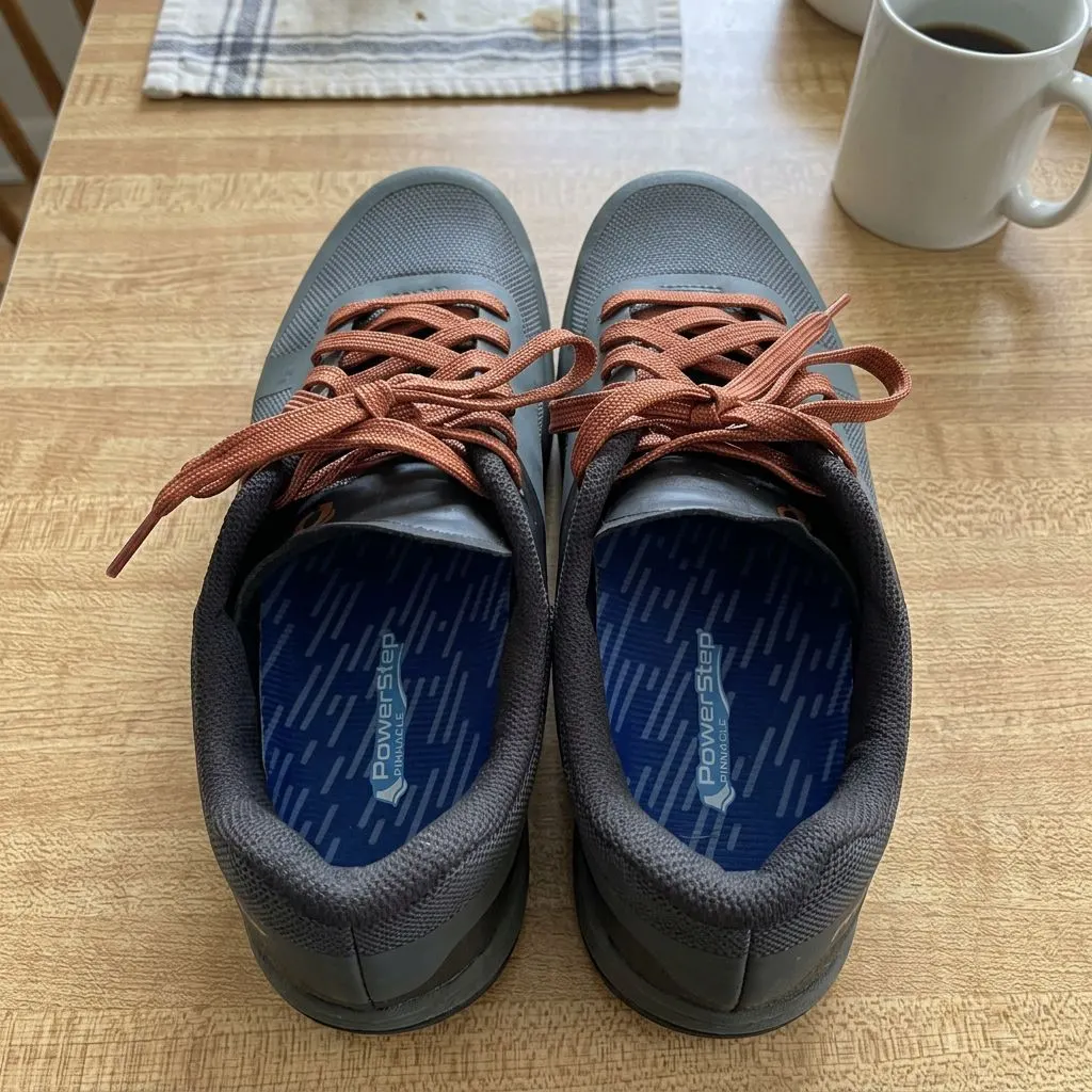 A pair of PowerStep Pinnacle insoles seated inside gray athletic shoes with brown laces