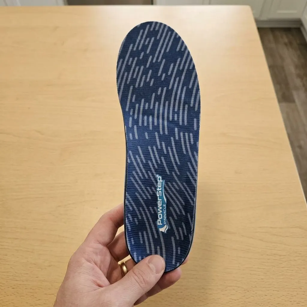 A PowerStep Pinnacle insole held up showing the textured blue top-cover fabric and branding