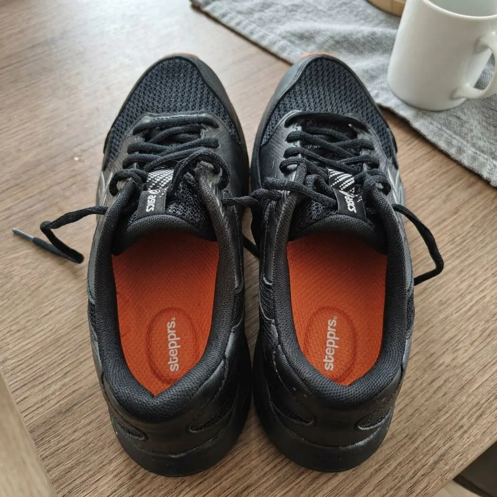 A pair of black sneakers with orange Stepprs insoles installed, showing the Stepprs branding printed on the heel cup