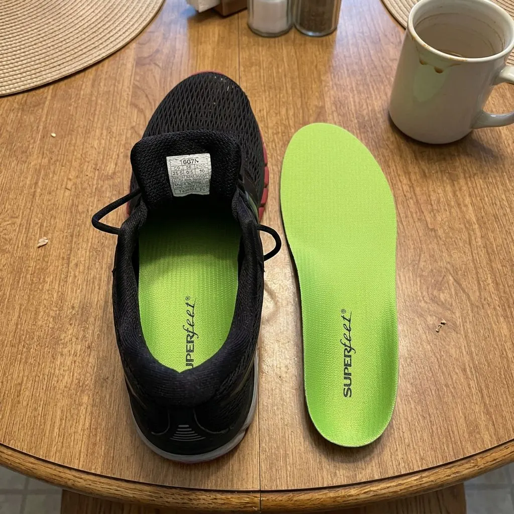 A Superfeet Green insole set beside a black athletic shoe with its stock insole still installed
