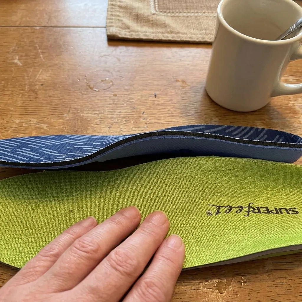 A Superfeet insole flipped to show its plastic shell base held next to a second Superfeet insole